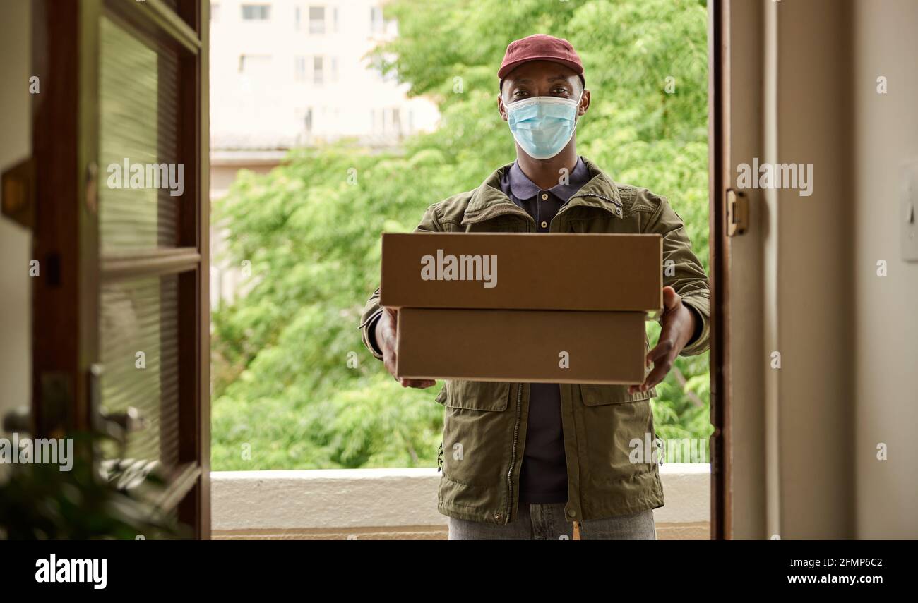 African courier in a mask holding up packages at a door Stock Photo