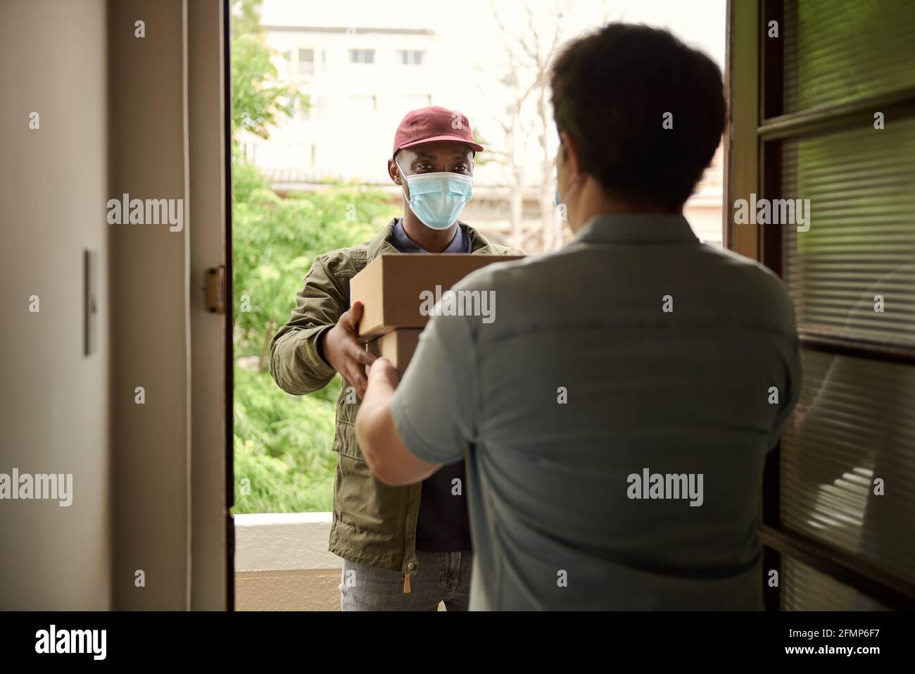 African courier in a mask delivering packages to a customer Stock Photo