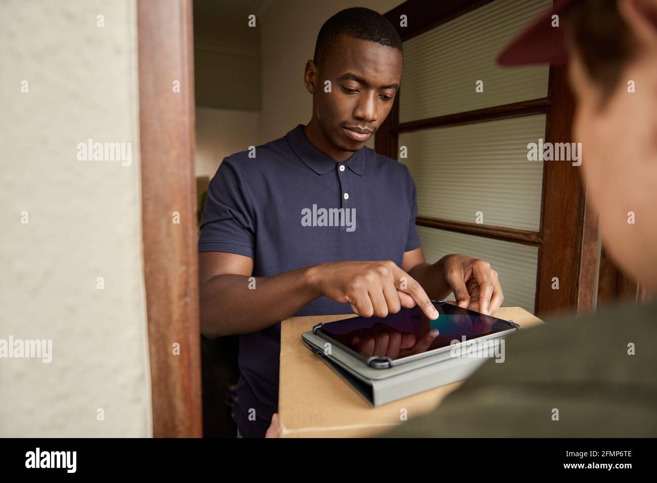 Young African man digitally signing a tablet for a delivery Stock Photo