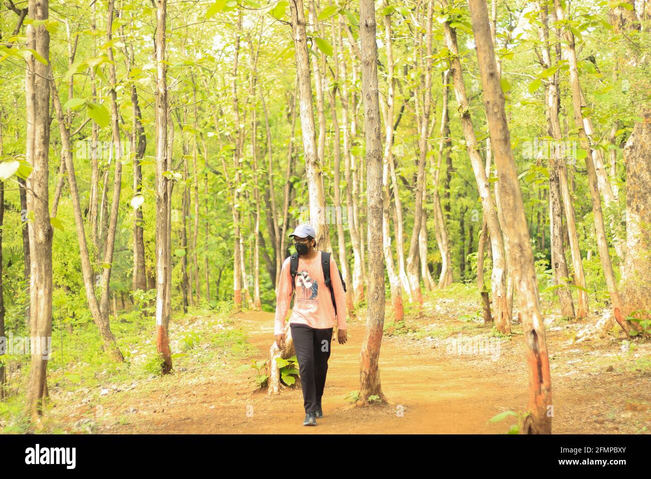 A 18-25 year old young Indian man wearing a cap and a mask amid covid-19 pandemic and walking freely and independently in a jungle. Stock Photo