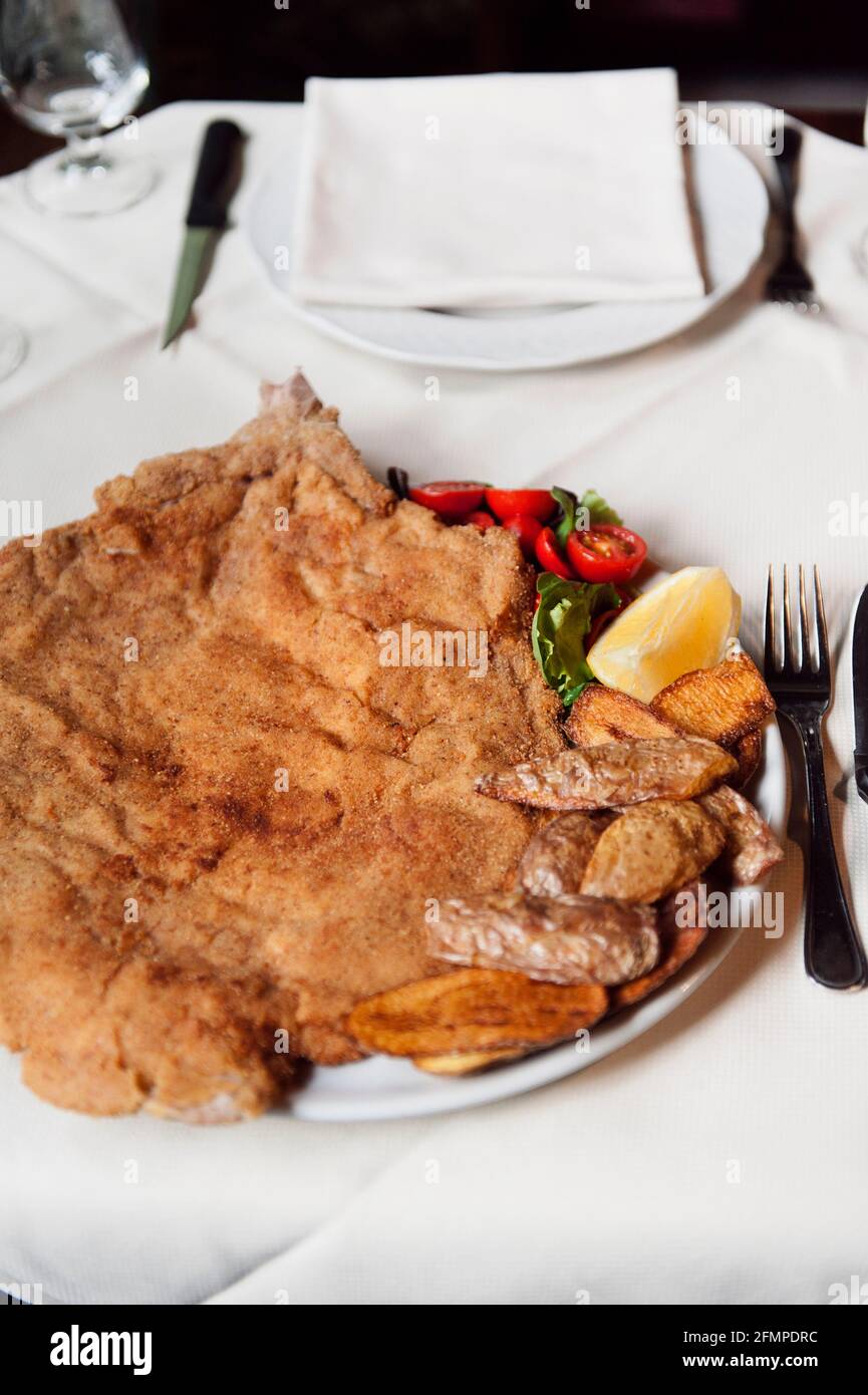 Cotoletta Milanese cooked by Restaurant Damm atra in Milano served with fried potatoes skind and tomatoes salad, Milan, Italy, Europe Stock Photo