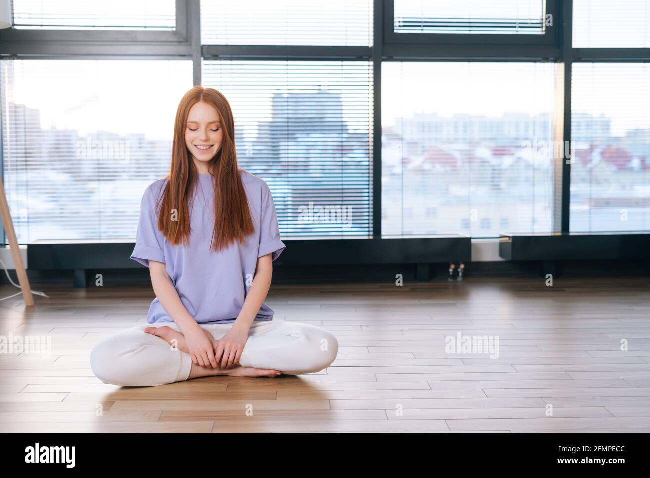 Portrait of smiling young relaxed woman meditating sitting on floor in ...