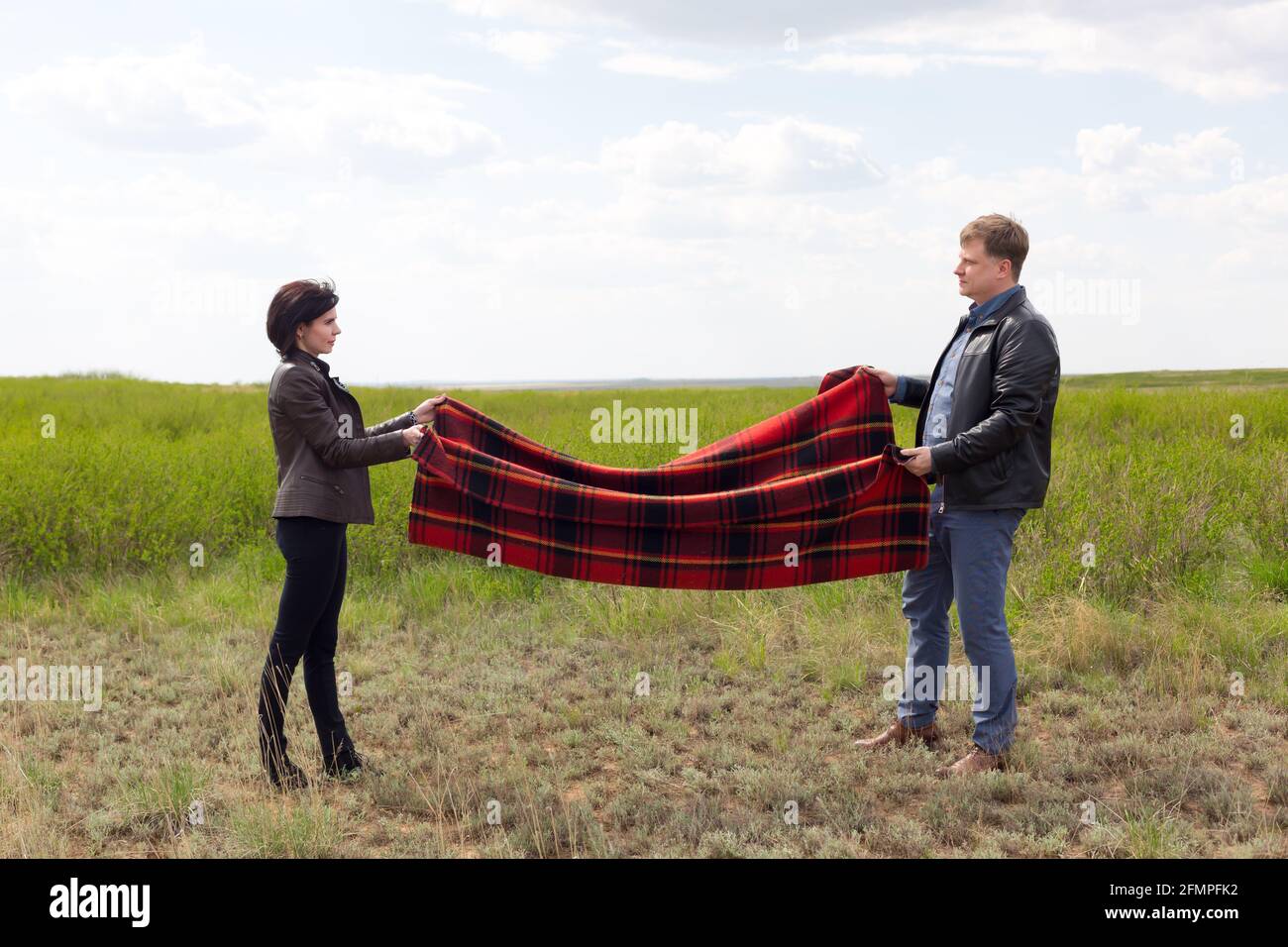 Man and woman lay a blanket on the ground for a picnic in nature Stock