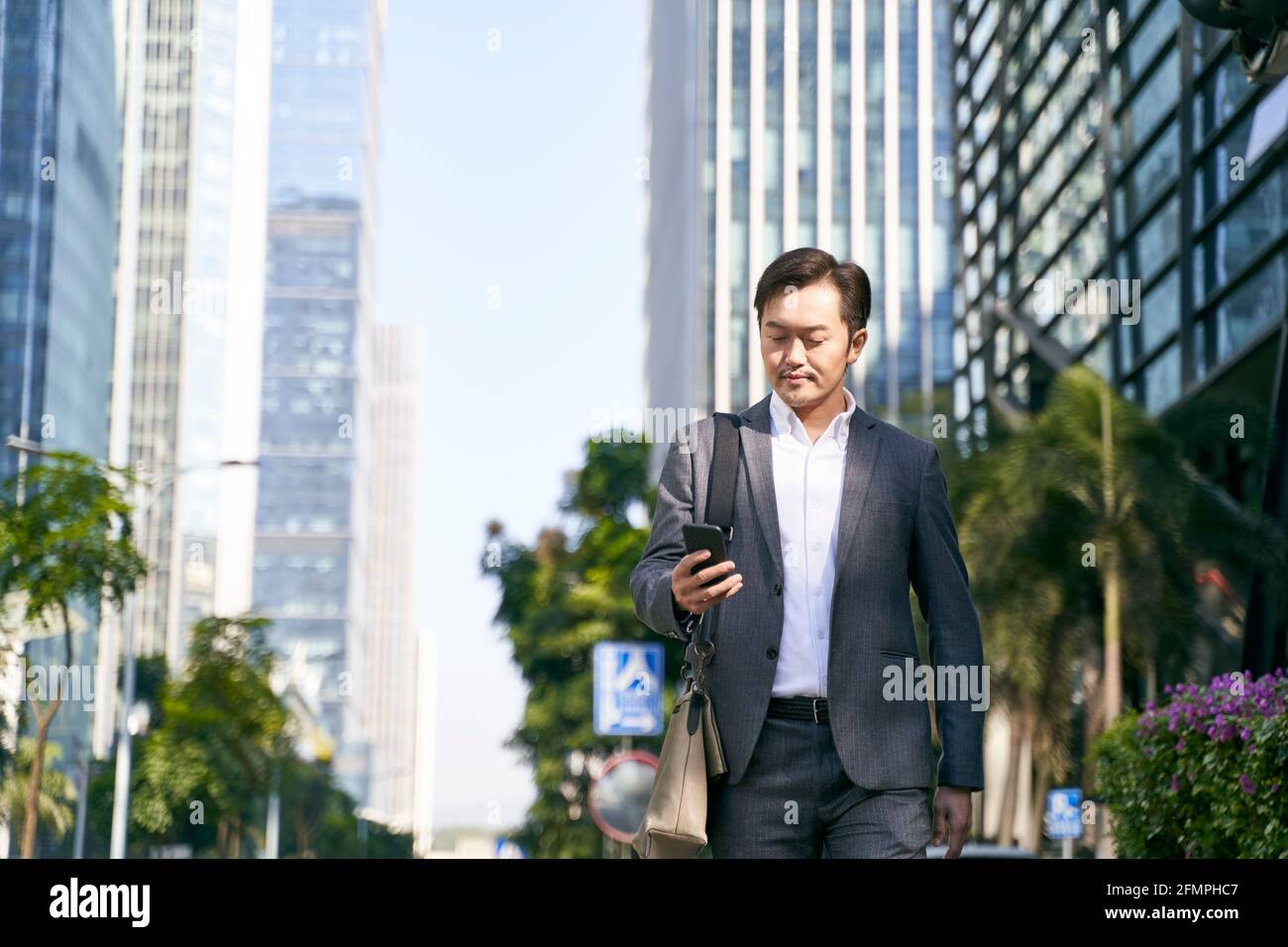 asian corporate executive looking at mobile phone while commuting to work in downtown of modern city Stock Photo