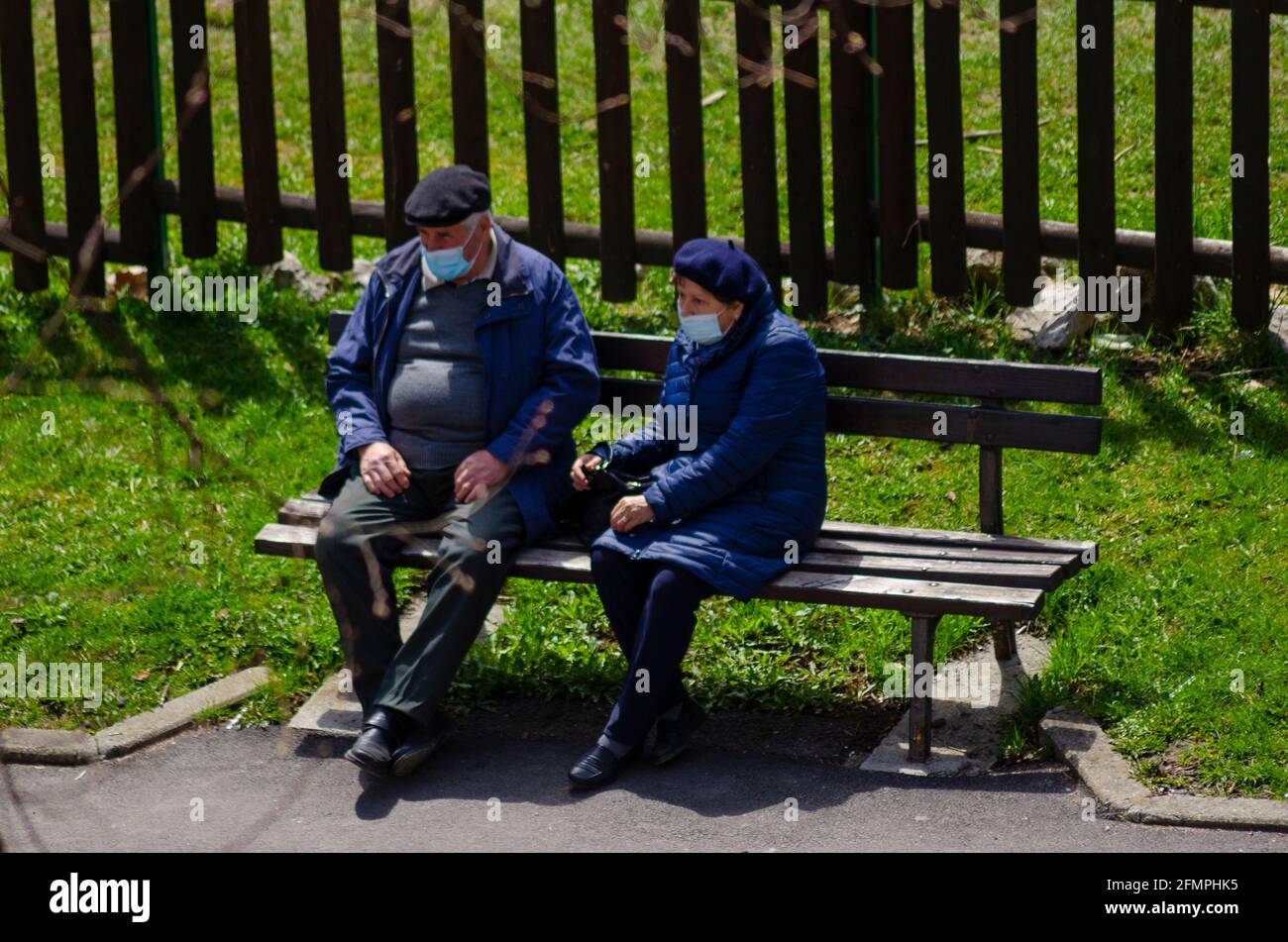 BRASOV, ROMANIA - 17 April 2021 - An elderly couple sit on a bench in Brasov, Romania. Despite an increasing amount of vaccinations, face masks are th Stock Photo