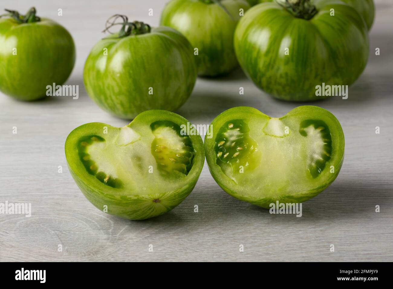 Whole and halved fresh green zebra tomato close up and tomatoes in the background Stock Photo