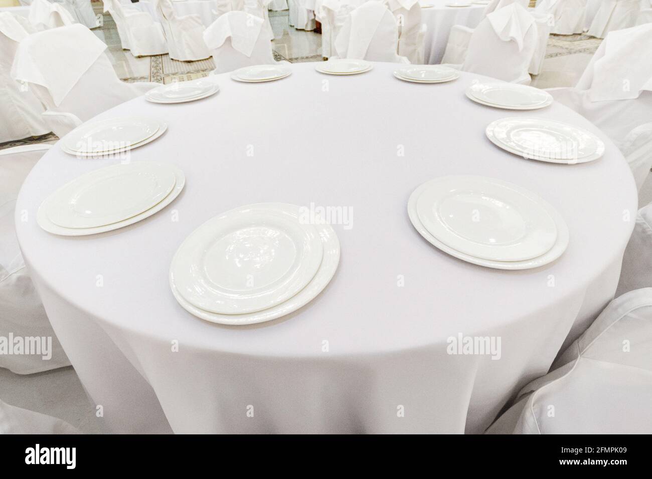 Empty white plates on a white tablecloth on a restaurant circle table. Restaurant table setting. Stock Photo