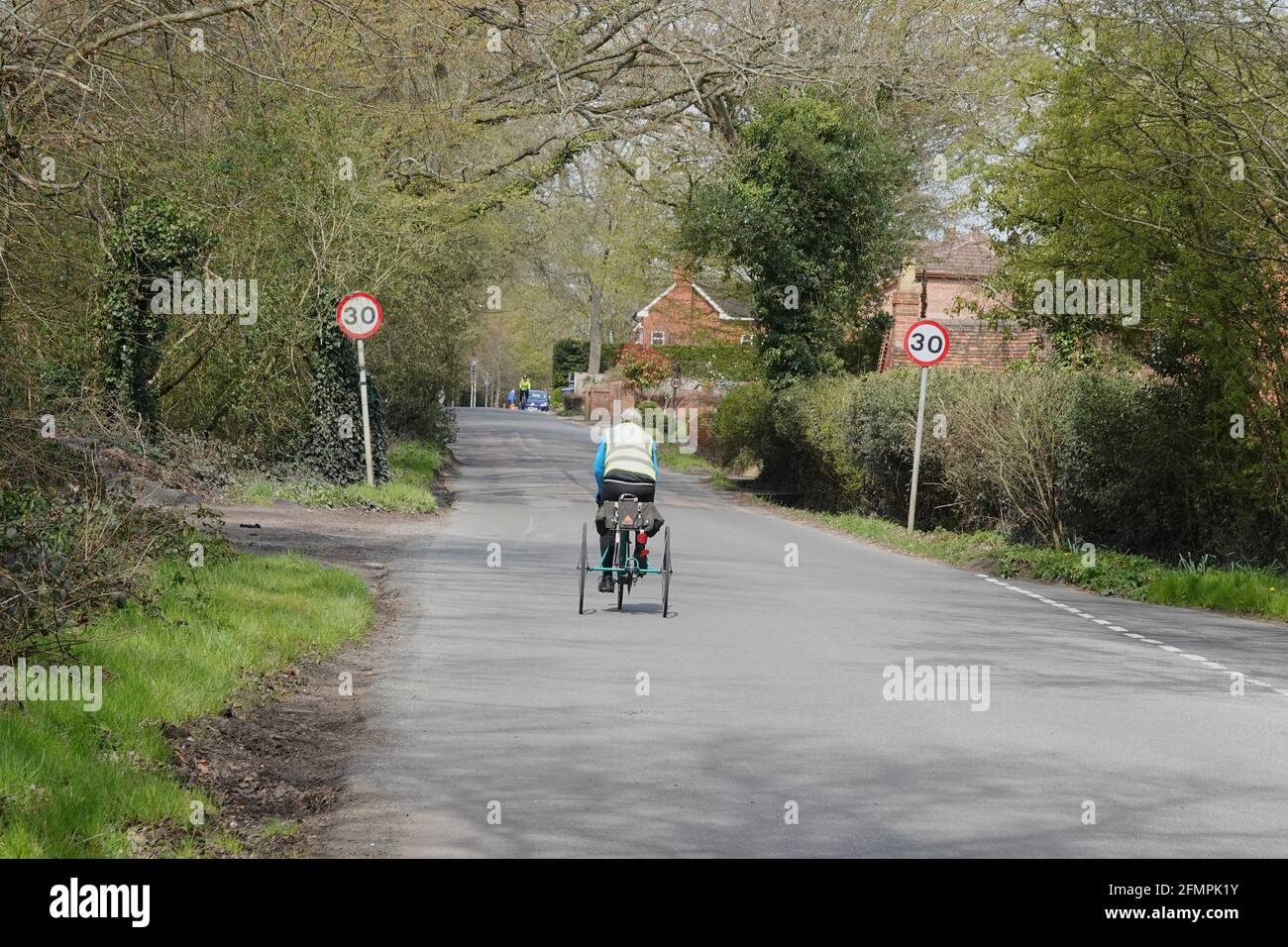 A senior man riding a tricycle along a country road in the UK Stock Photo