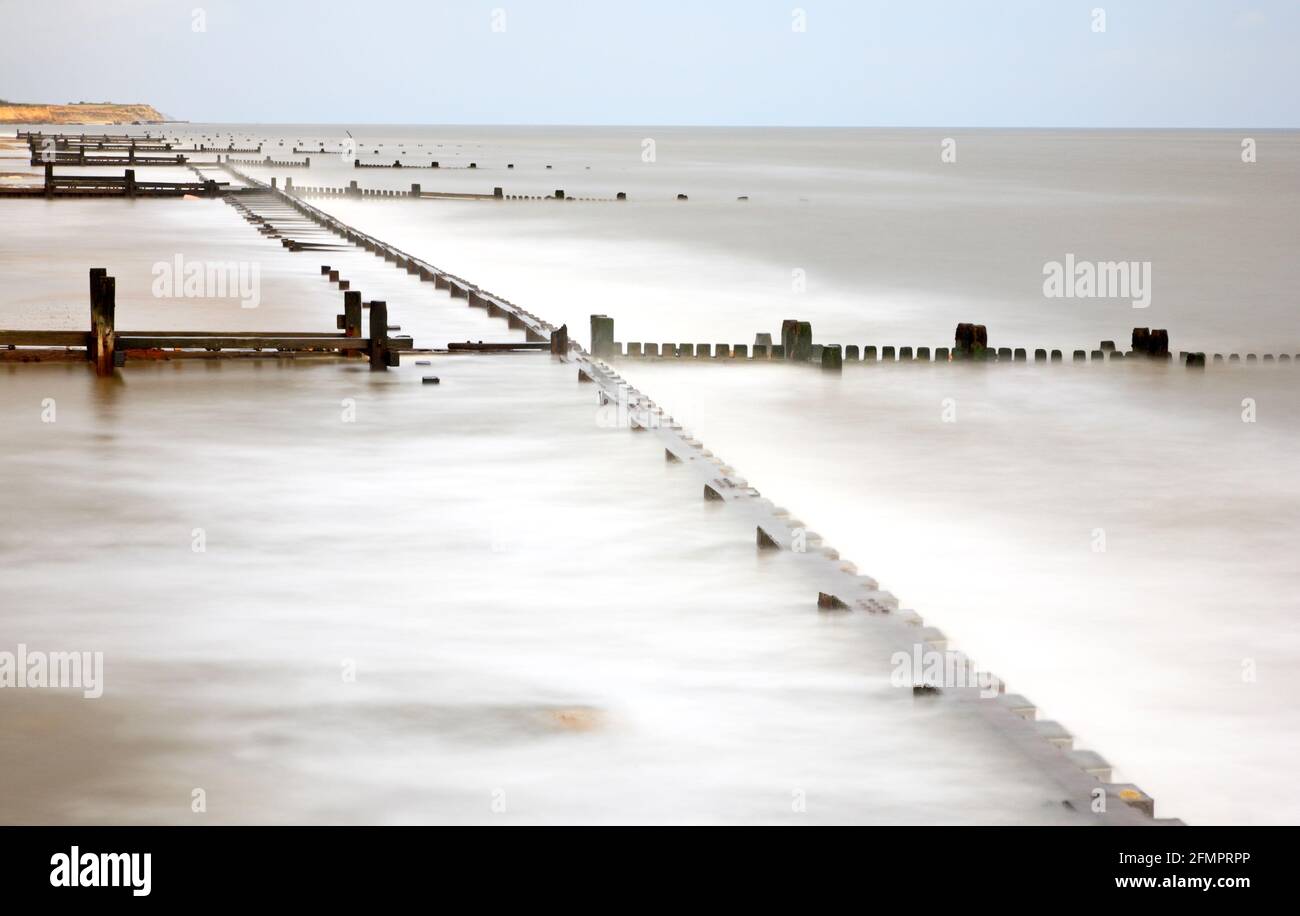 A seascape with old breakwaters utilizing a long exposure to reveal a wave flattened shoreline at Cart Gap, Happisburgh, Norfolk, England, UK. Stock Photo
