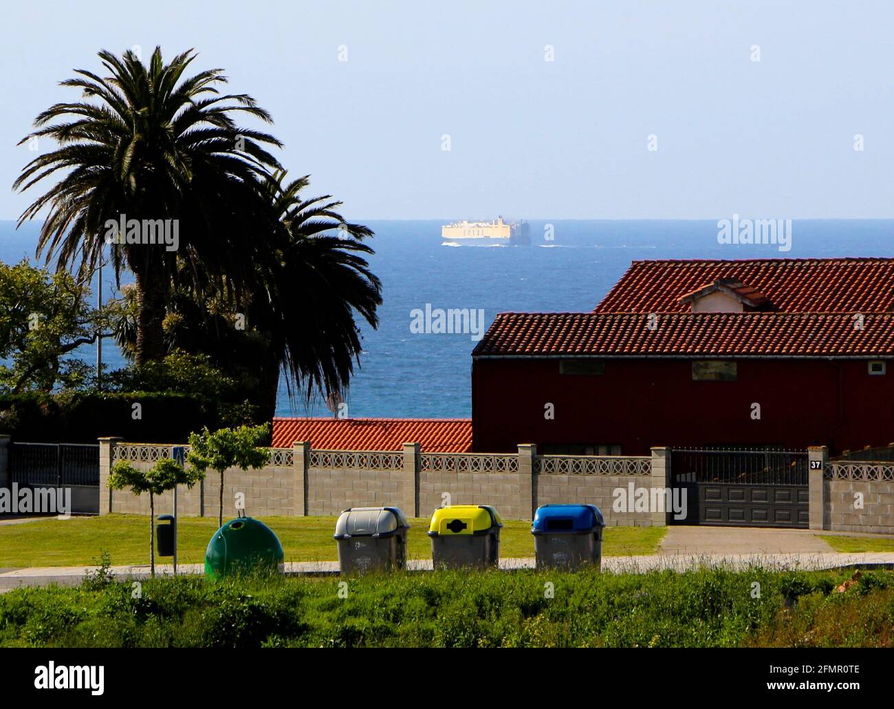 A line of rubbish bins for glass general waste plastic and papr with a sea view and a ship
