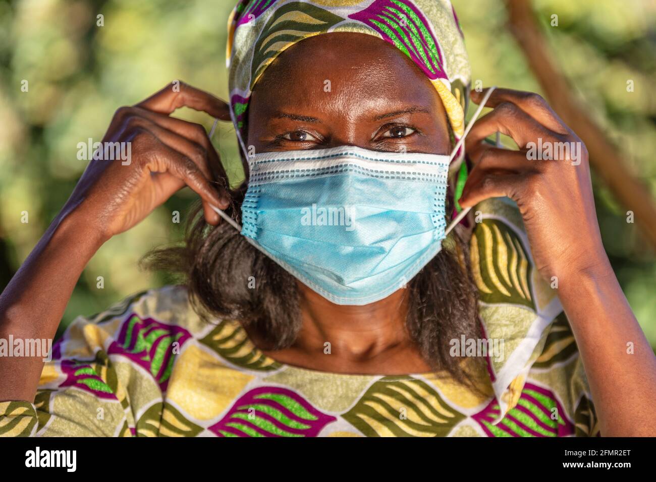 African middle aged woman, female in Africa, wearing traditional clothes and putting on face mask in Coronavirus COVID-19 pandemic Stock Photo