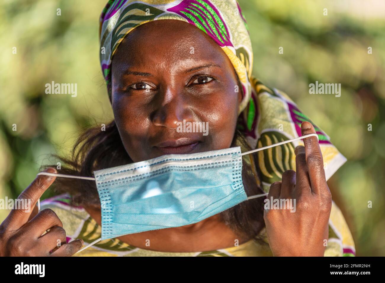 African middle aged woman, female in Africa, wearing traditional clothes and taking off face mask in Coronavirus COVID-19 pandemic Stock Photo
