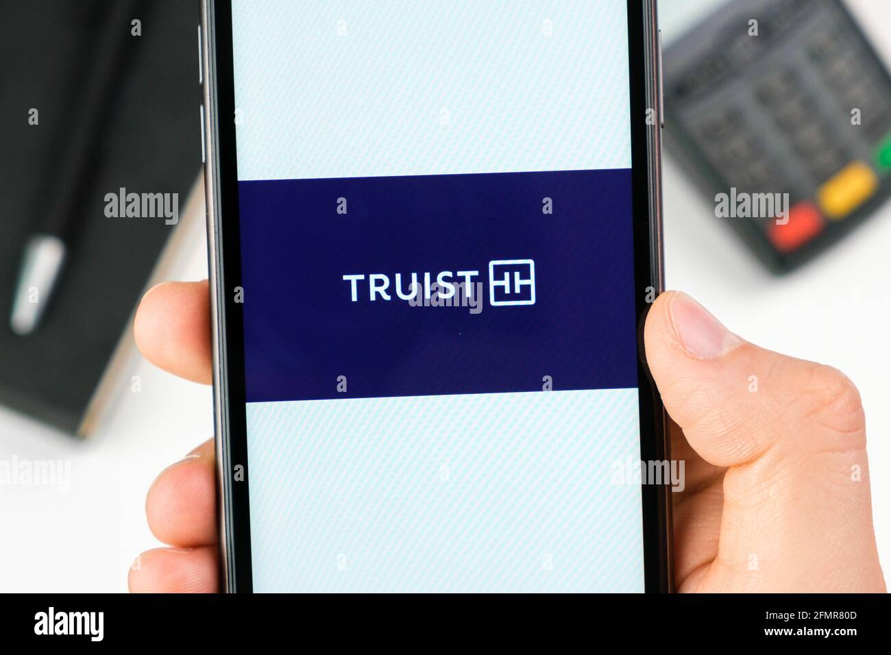 Truist bank logo on the smartphone screen in mans hand on the background of payment terminal, May 2021, San Francisco, USA Stock Photo