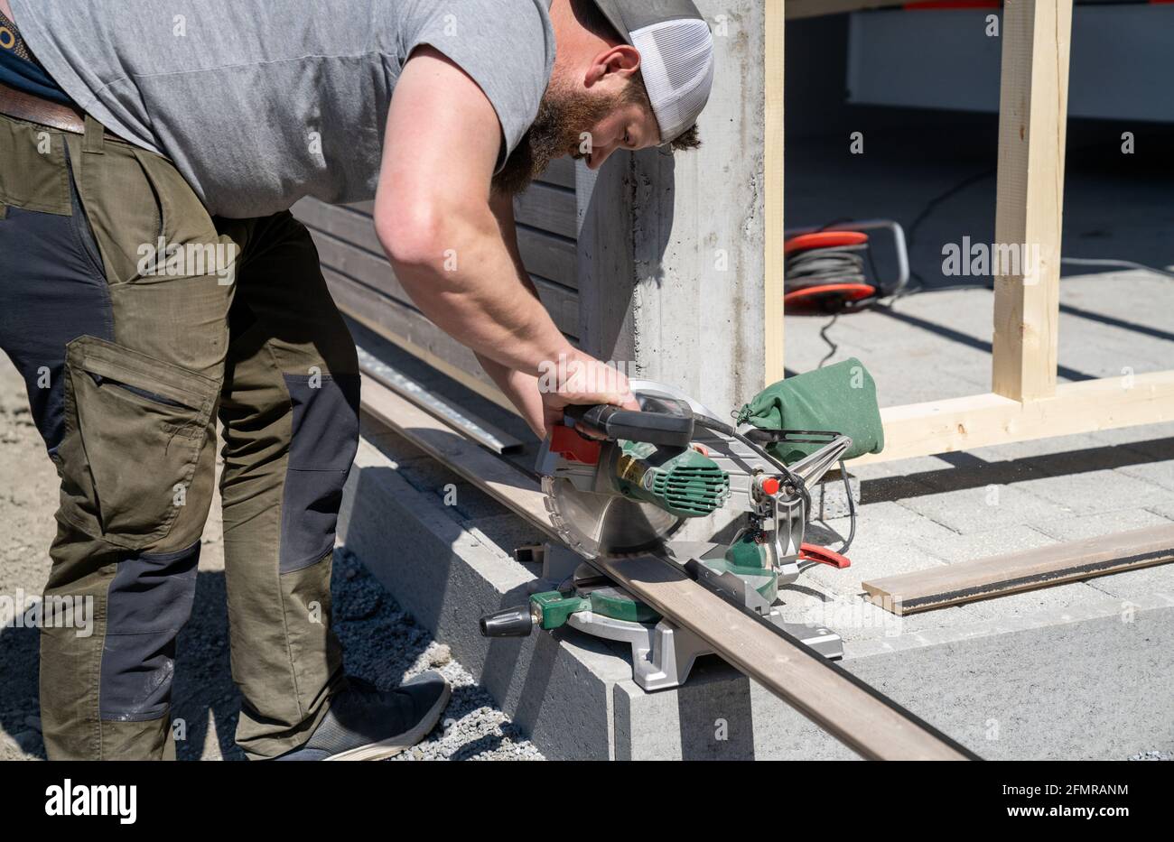 A tough construction worker cuts wooden siding with a tilt saw while