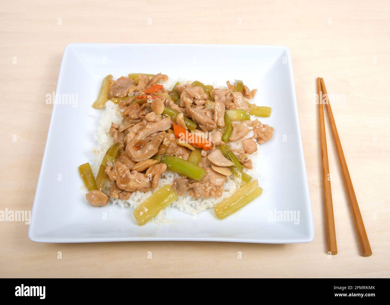 Square plate with Almond Chicken over rice on a wood table with chop ...