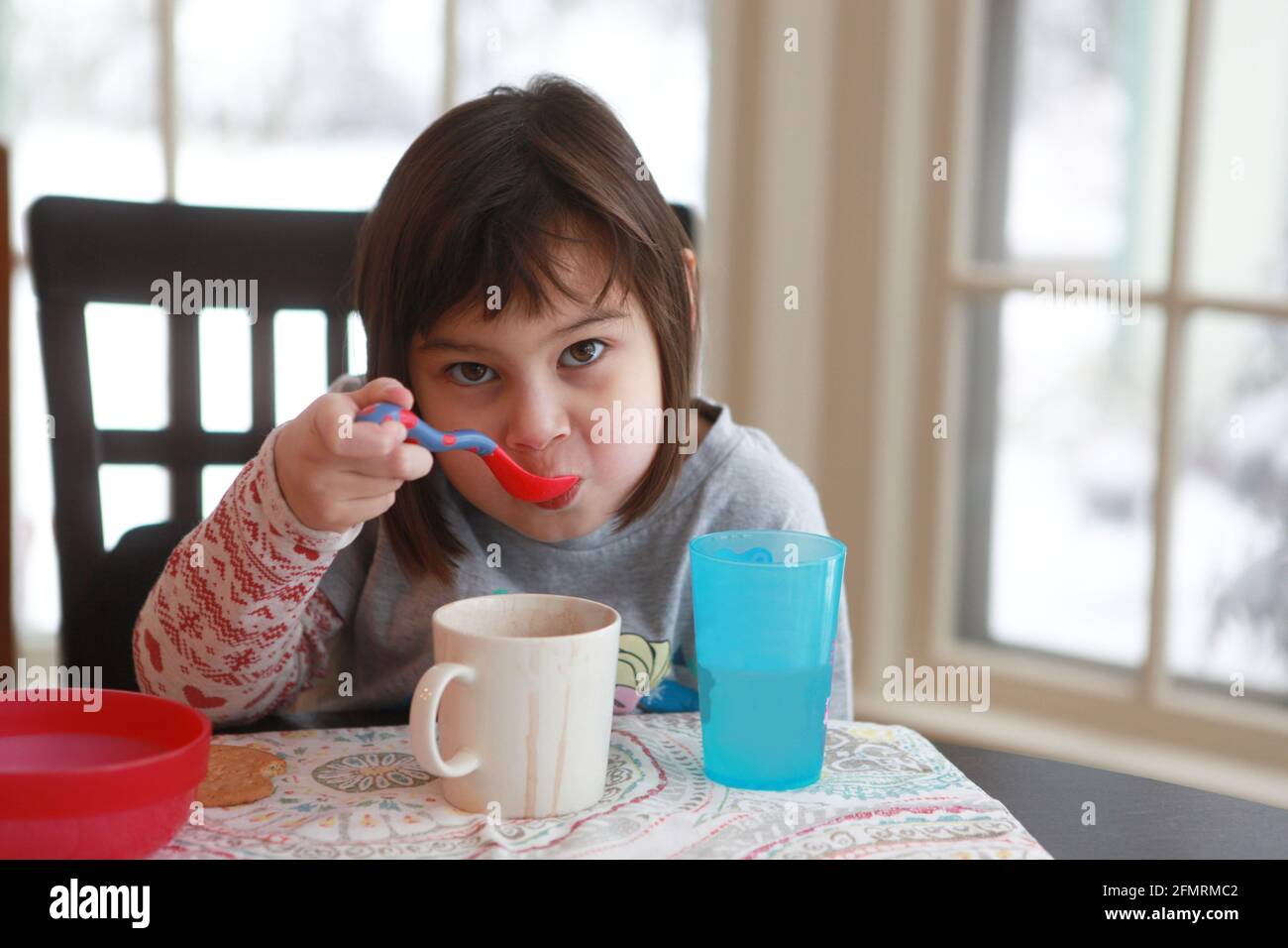 Little girl enjoying some hot chocolate in her kitchen on a snowy day. Stock Photo
