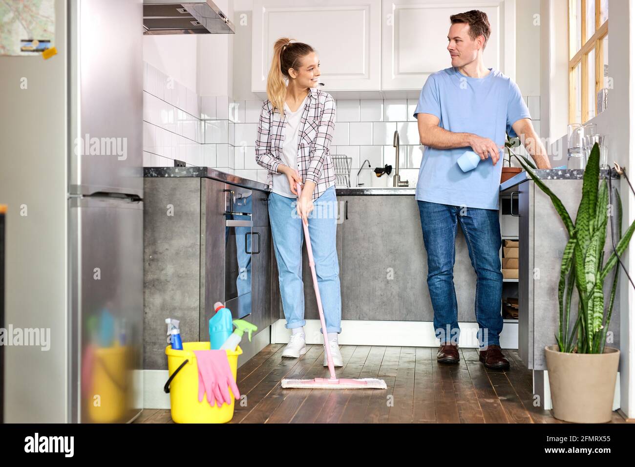 Young Janitors Cleaning Kitchen And Mopping Floor At Home, Caucasian Man And Woman In Casual Weae Enjoy Housekeeping, Cleaning Flat Apartment Stock Photo