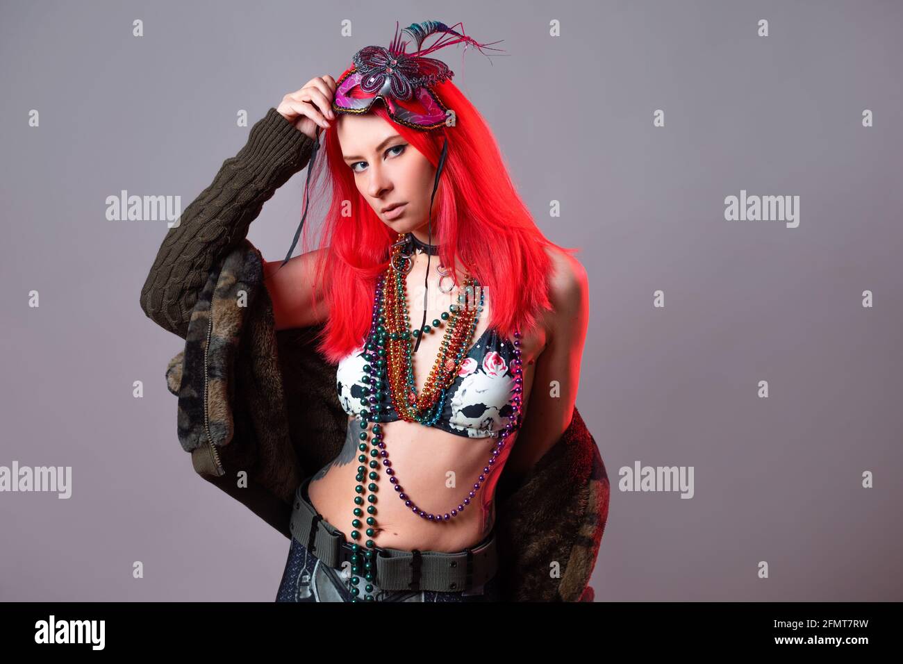 Young woman with bright pink hair in a Mardi Gras costume, beads and a mask with feathers, crazy kitsch outfit. Stock Photo
