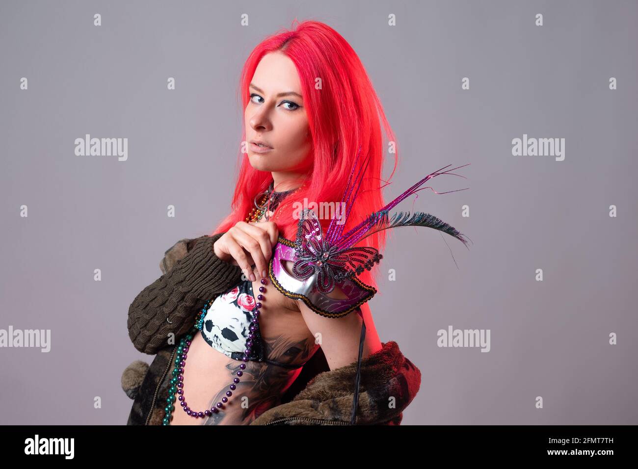 Young woman with bright pink hair in a Mardi Gras costume, beads and a mask with feathers, crazy kitsch outfit. Stock Photo