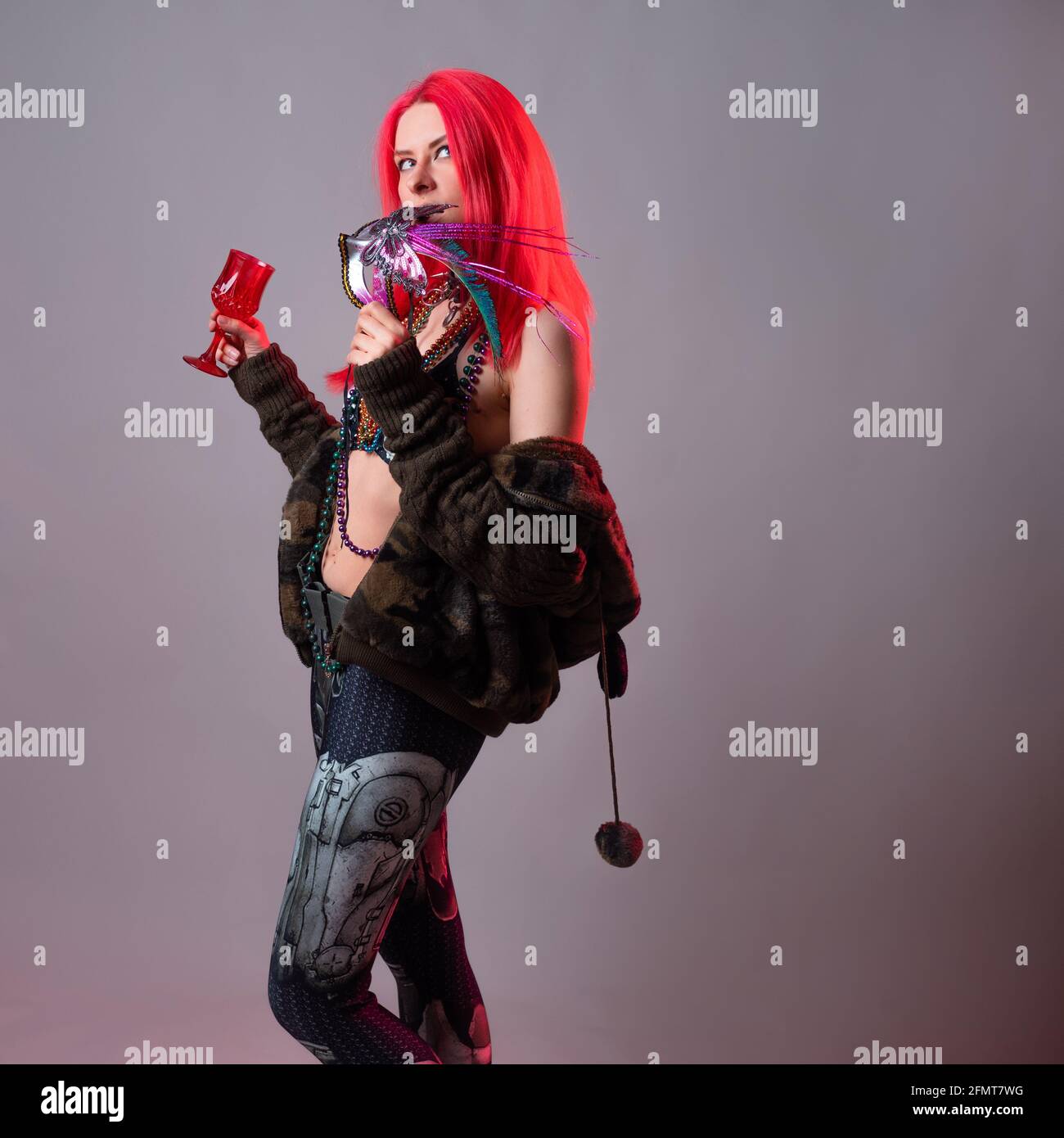 Young woman with bright pink hair in a Mardi Gras costume, beads and a mask with feathers, crazy kitsch outfit. Stock Photo