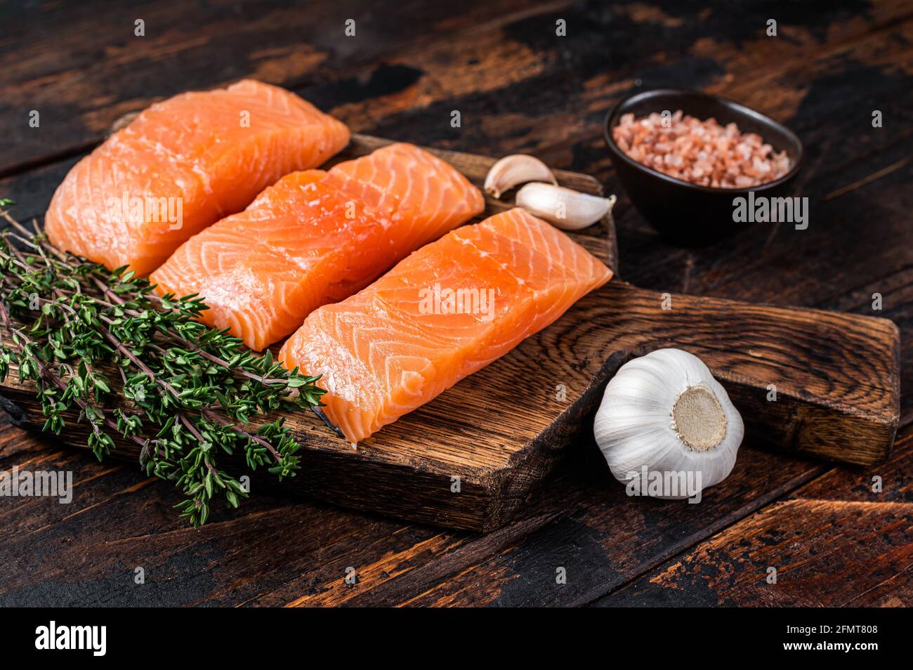 Fresh Raw salmon fish fillet steaks on wooden board with thyme. Dark ...