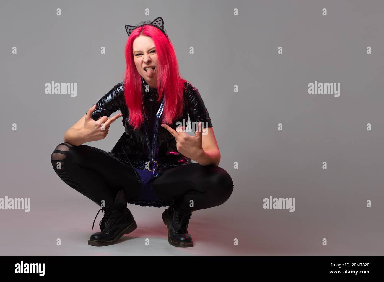 A cheerful and kawaii bully with kitten ears, a young woman with pink hair squatted down. Stock Photo