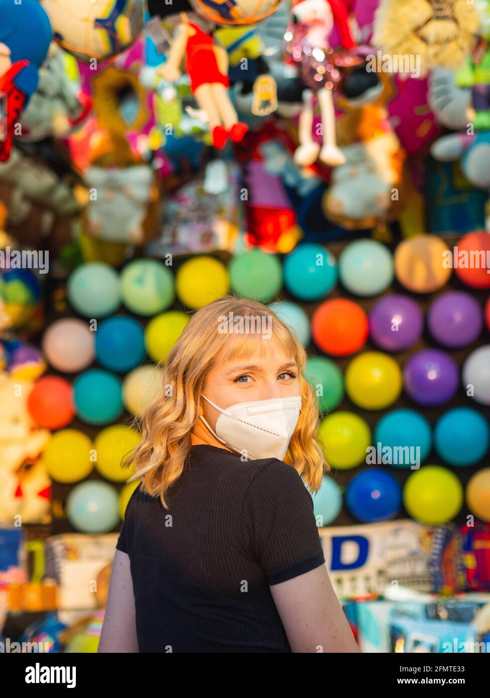 Blonde woman in a mask playing pop balloons with darts game Stock Photo -  Alamy