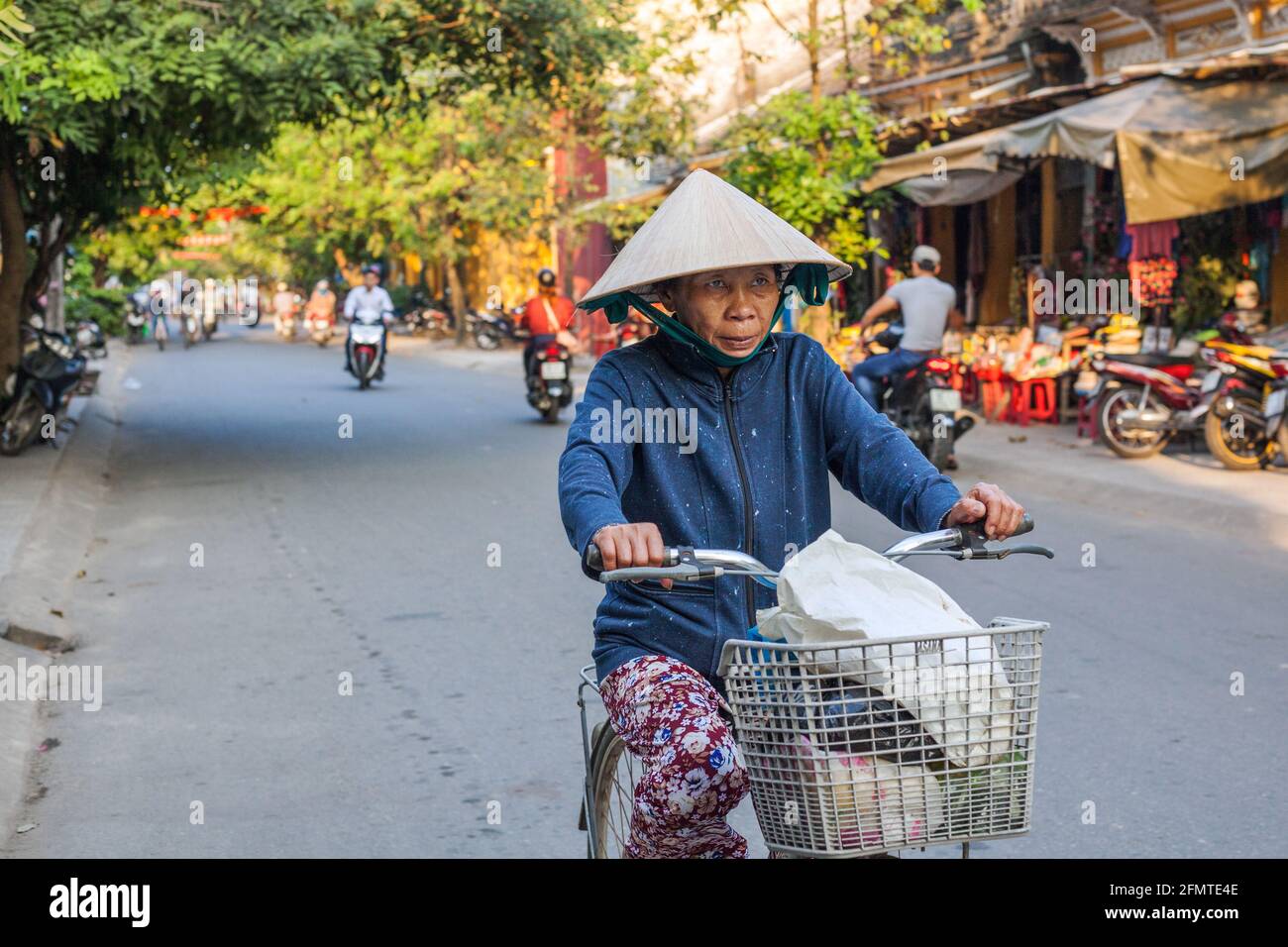 Elderly Vietnamese lady wearing conical hat riding a bicycle, Hoi An, Vietnam Stock Photo