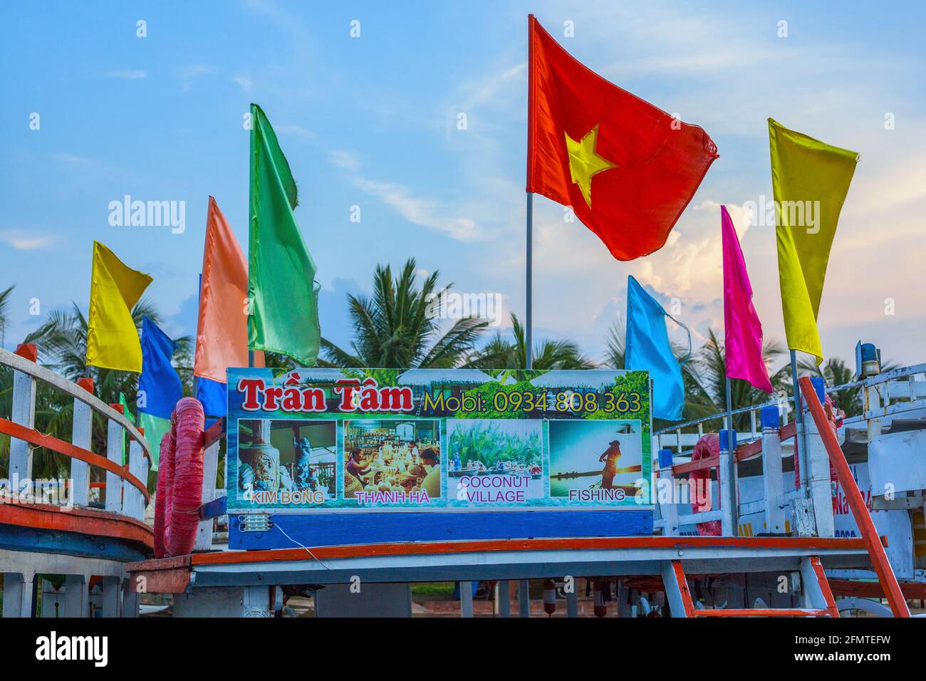 Vietnam flag and other colourful flags flying on top of boat moored on riverside offering tourist cruises, Hoi An, Vietnam Stock Photo