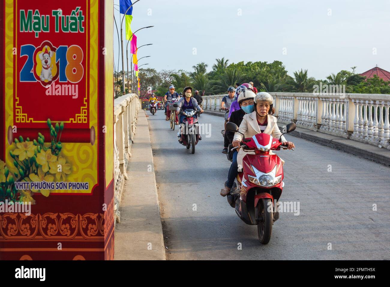 Elderly Vietnamese female driving scooter across bridge in old town, Hoi An, Vietnam Stock Photo
