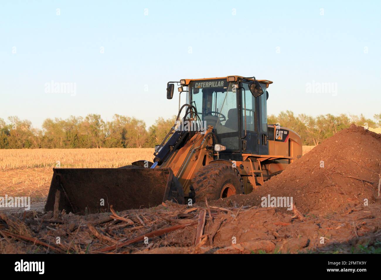 A Caterpillar Front End loader in a field with a pile of dirt  ready for work north of Lyons Kansas USA on a colorful day. Stock Photo