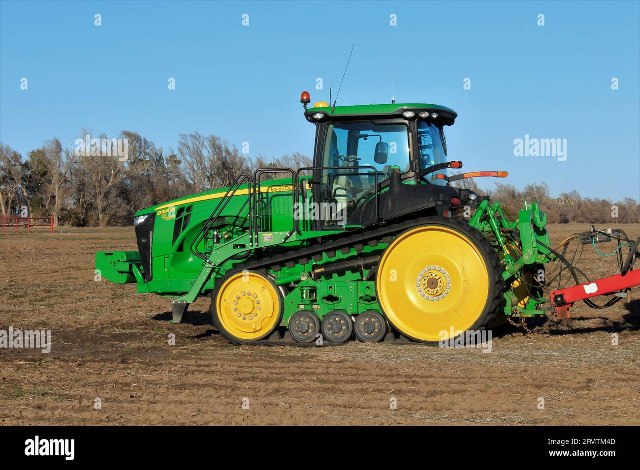 A John Deere track tractor in a farm field with blue sky and tree's out in the country. Stock Photo