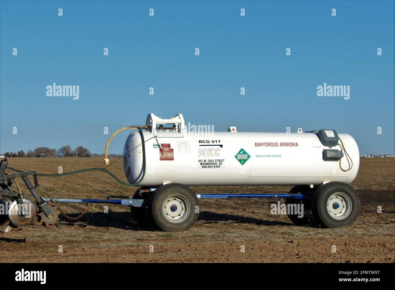 MKC Anhydrous Ammonia tank in a farm field shot closeup hooked up behind a farm tractor on a colorful day in Kansas. Stock Photo
