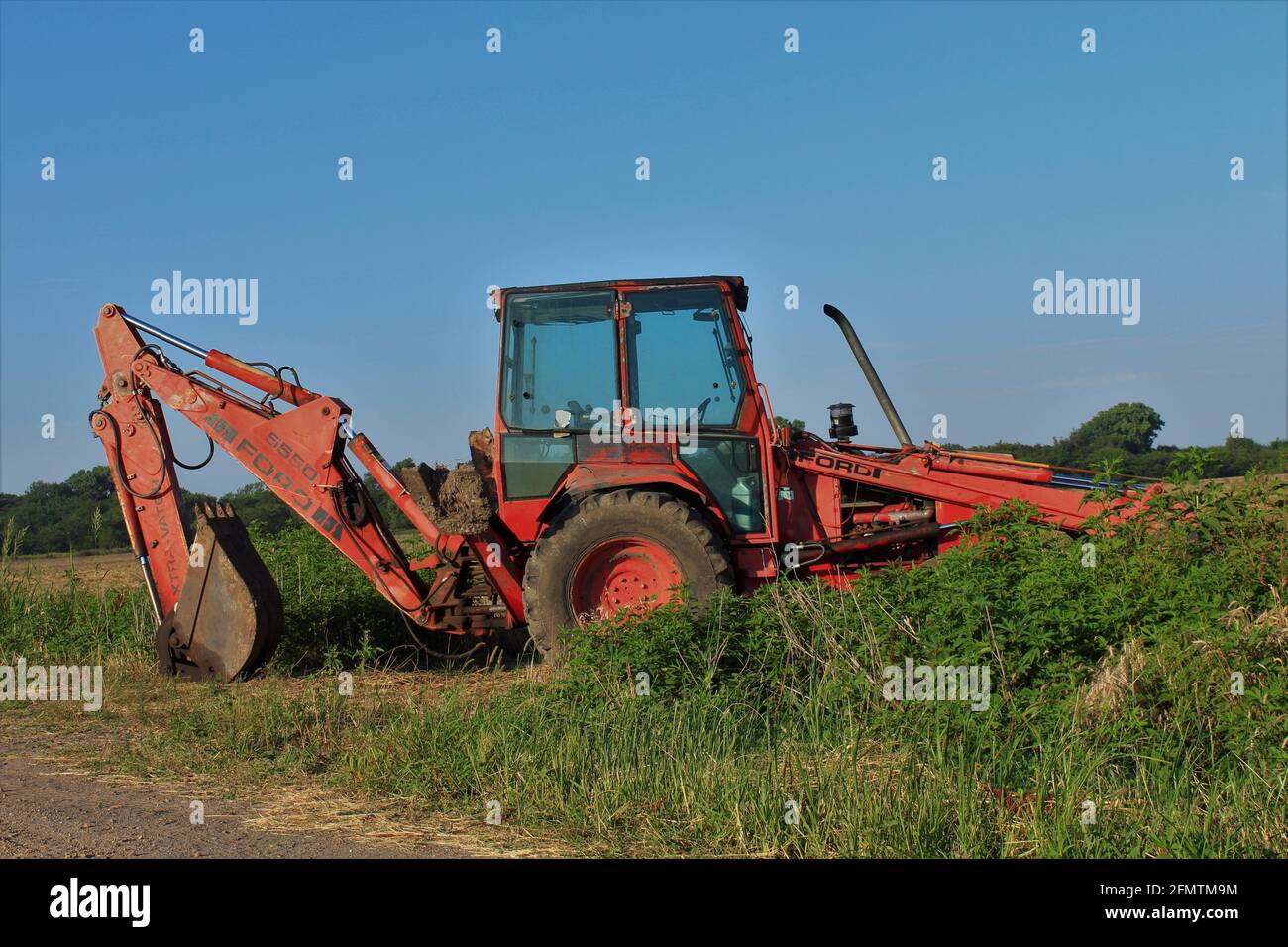 Ford Tractor with a front end loader and backhoe parked by a farm field ready for work that's out in the country in Kansas. Stock Photo