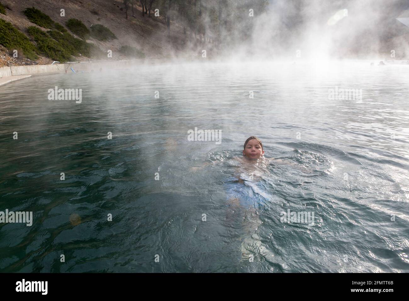 A boy floats in a Trinity Hot Springs pool with steam rising Stock Photo