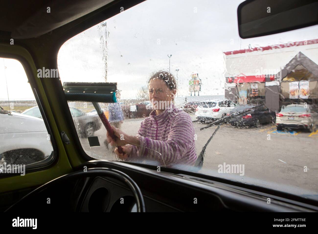 A woman cleans the windshield of VW camper van during roadtrip Stock Photo
