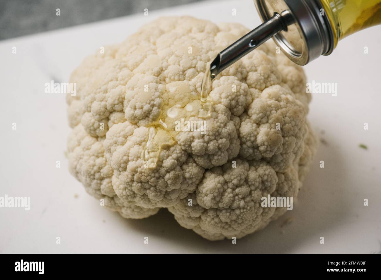 Pouring olive oil over a head of cauliflower Stock Photo
