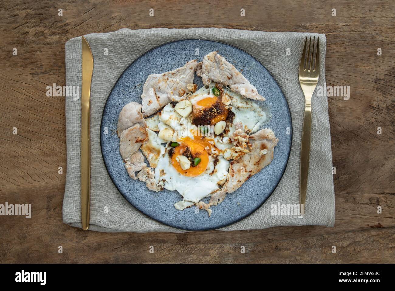 Breakfast with Fried egg, Roasted pork sprinkle garlic, chili in plate with Knife and fork on old wooden table. Selective focuse. Stock Photo