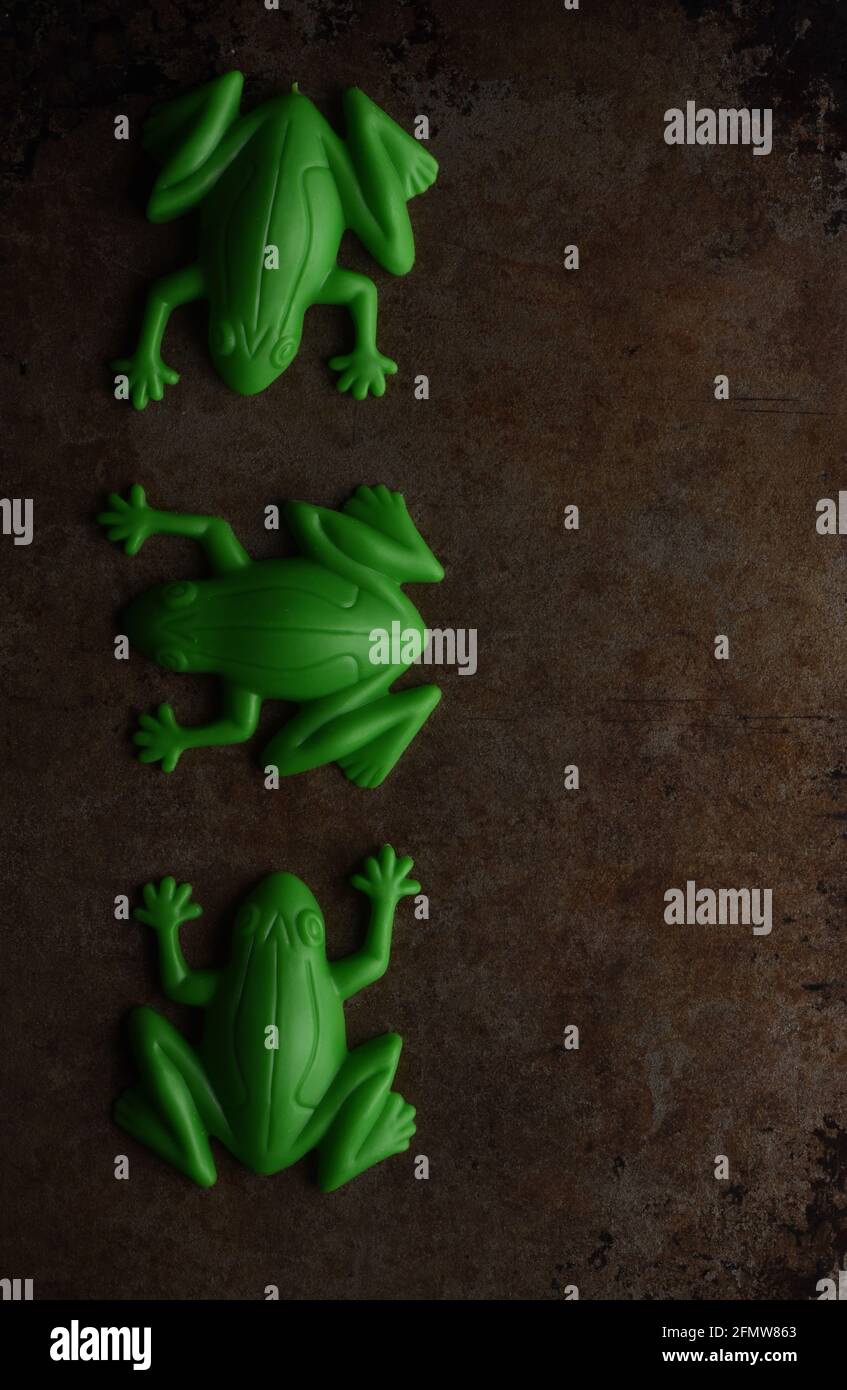 A still life studio vertical image on a tarnished metal background of three  green plastic toy frogs Stock Photo - Alamy