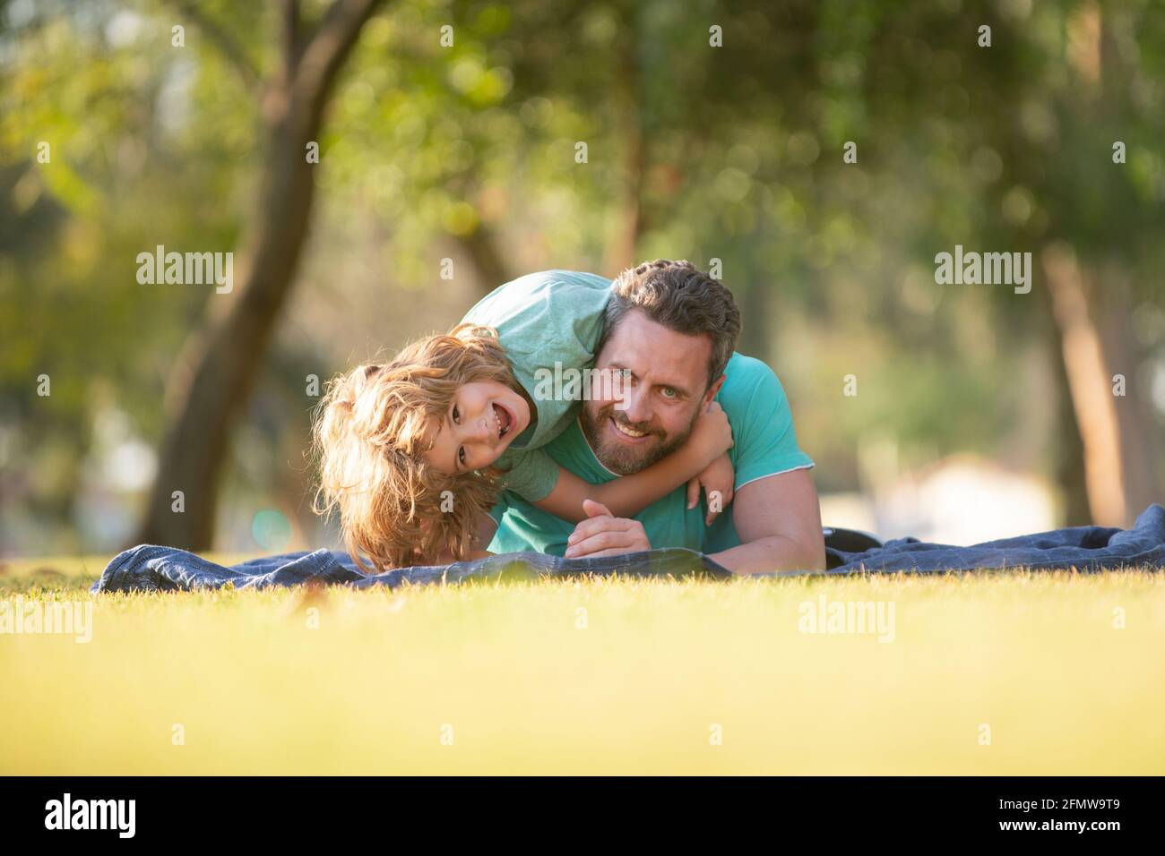 Handsome father piggybacking son playing on nature, daddy holding riding on back adorable cheerful kid boy enjoy active game. Child embracing and Stock Photo