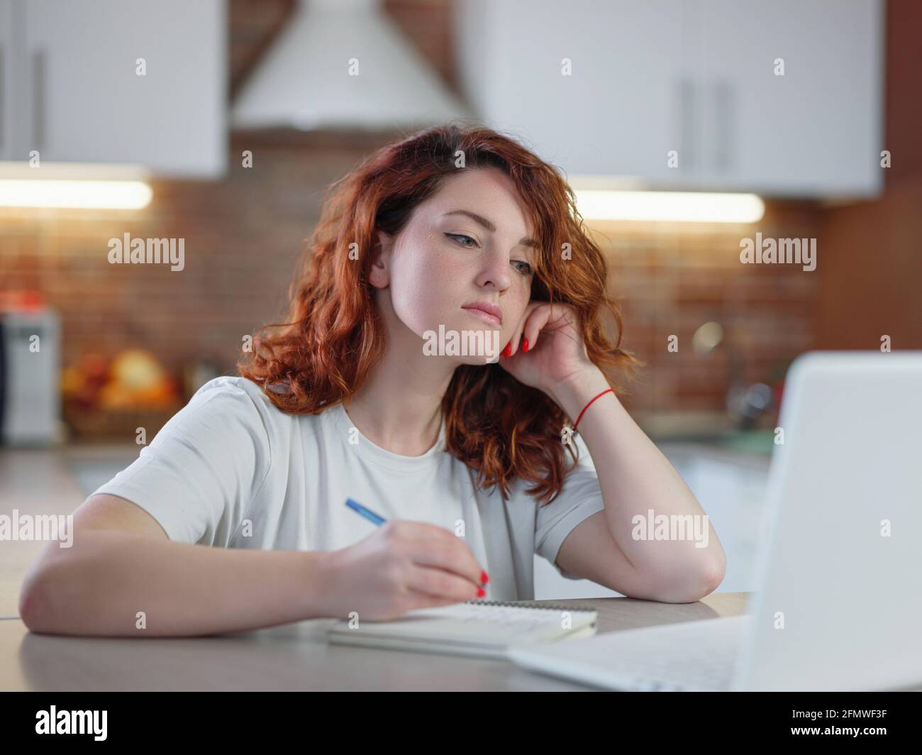 A beautiful young redheaded woman sits in the kitchen at the table with ...