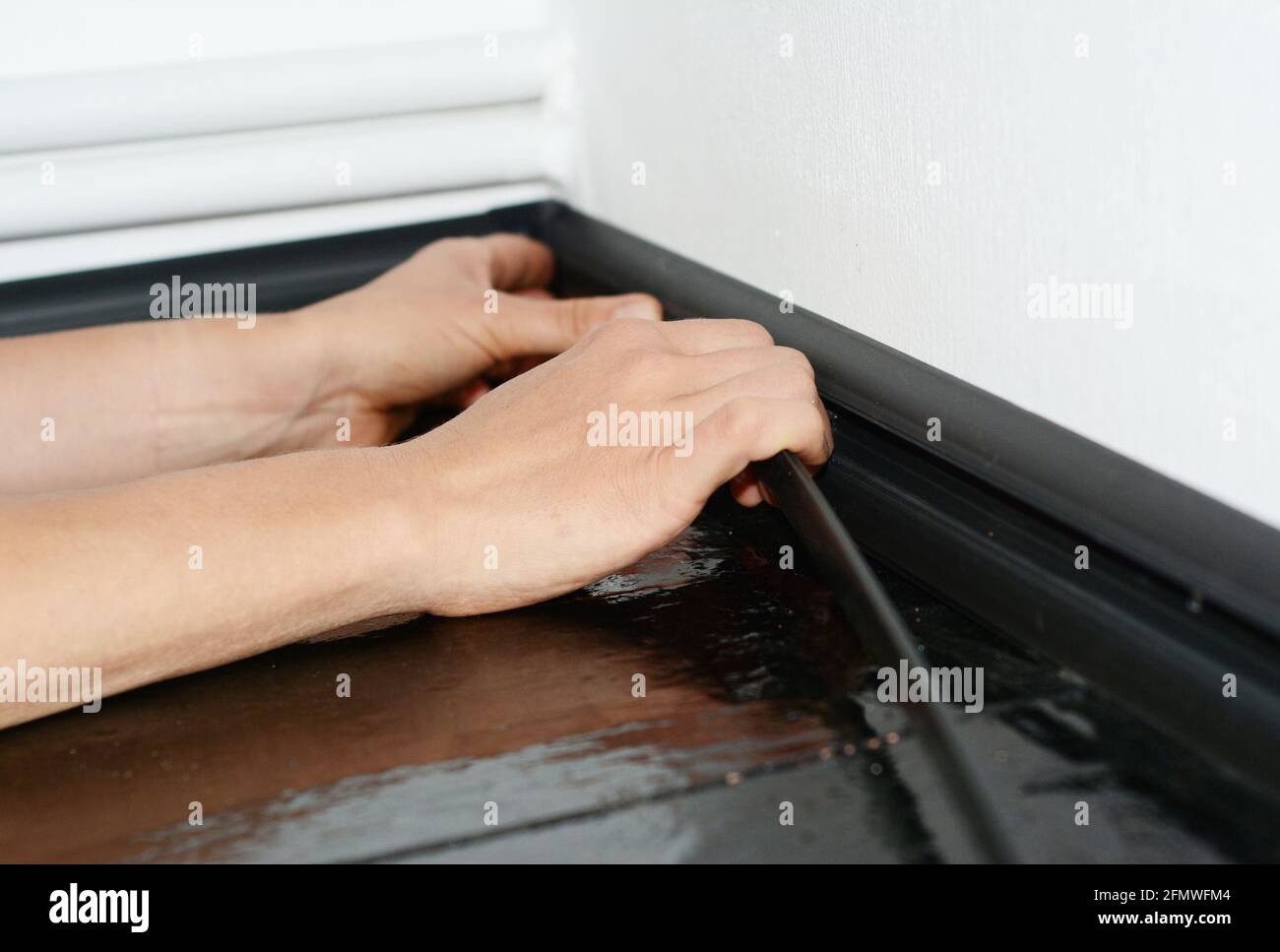 A man is installing a black plastic skirting board to hide cables and