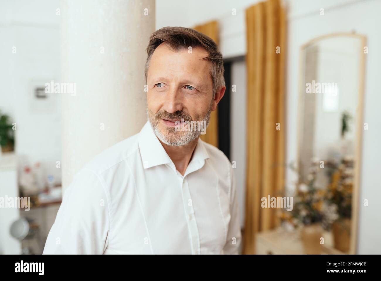 Middle-aged man standing daydreaming with serious faraway expression as he looks aside indoors at home in a close up head and shoulders Stock Photo