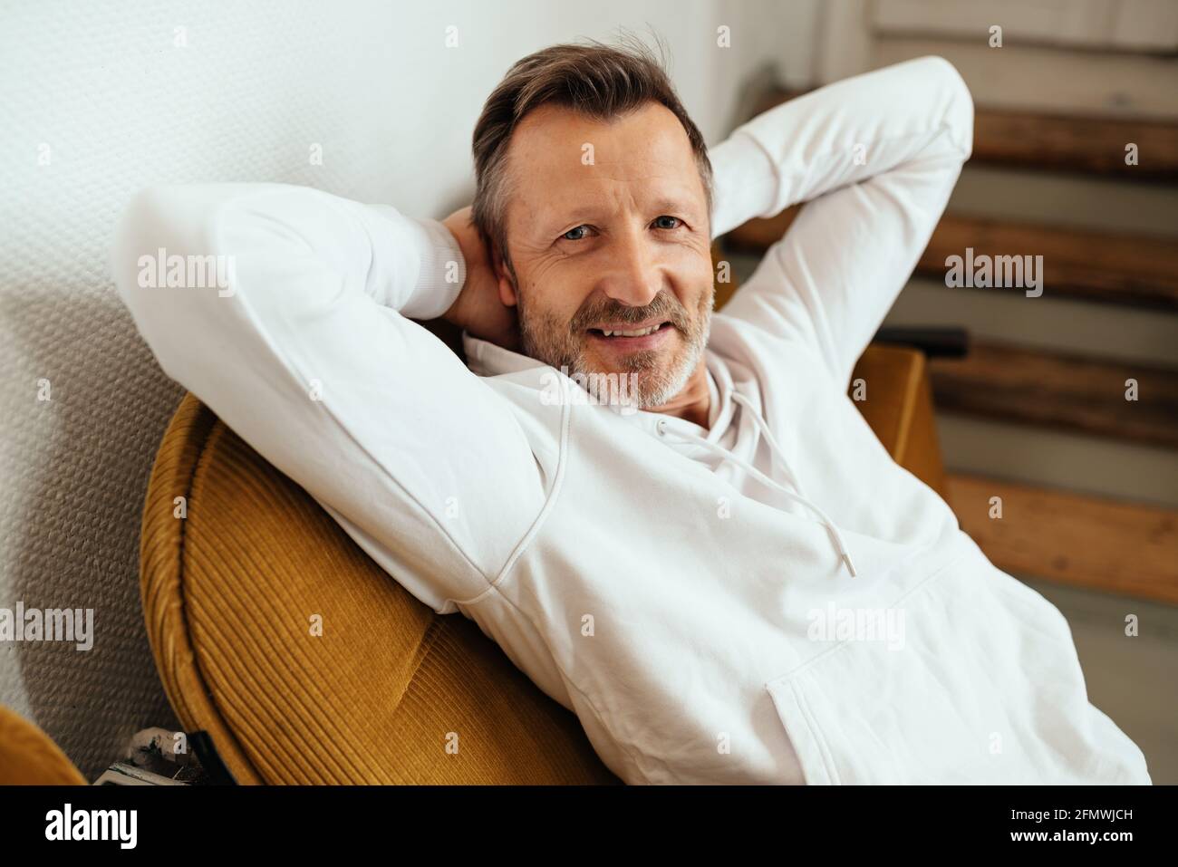 Laid-back man relaxing in a chair with hands behind his head turning to smile quietly at the camera in a close up high angle view Stock Photo