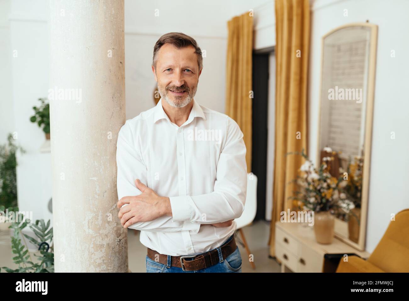 Confident relaxed man leaning on an interior cement pillar smiling at the camera with an intense expression as though listening Stock Photo