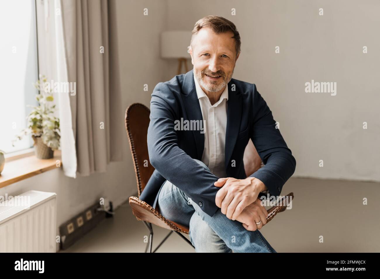 Interested attentive businessman leaning forwards towards the camera listening with a quiet smile and intense stare as he sits indoors in a leather ch Stock Photo