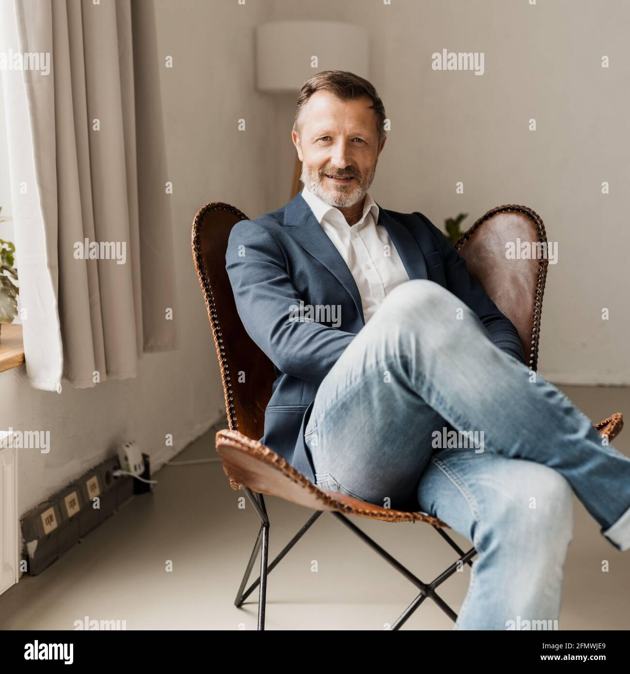 Relaxed stylish modern businessman sitting in a leather chair looking at the camera with a quiet smile and interested gaze in square format Stock Photo