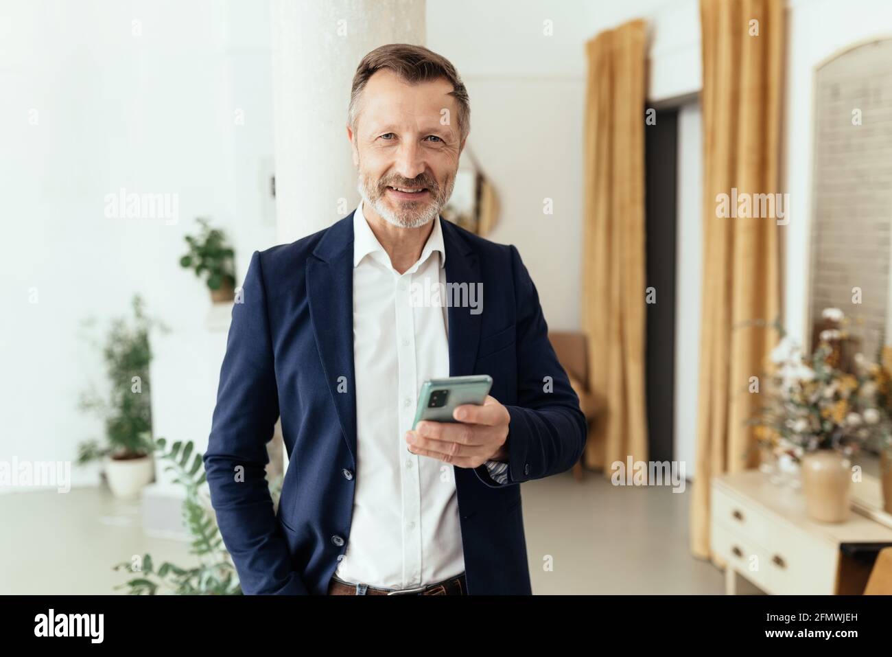 Businessman looking up with a smile at the camera while holding his mobile phone in his hand as though interrupted in what he was doing Stock Photo