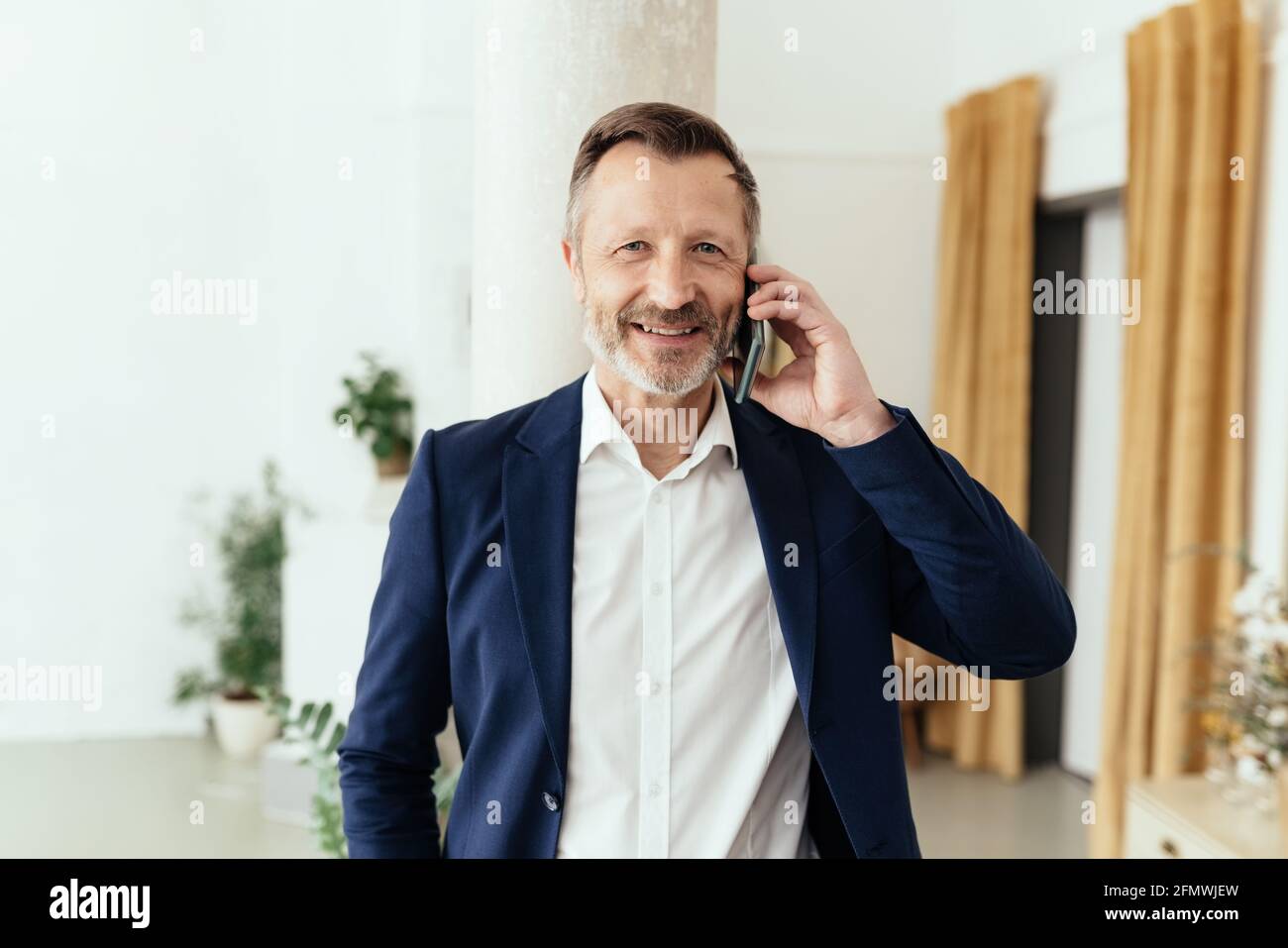 Smart middle-aged businessman chatting on his mobile phone listening to the call with a quiet thoughtful smile in a close up indoor portrait Stock Photo