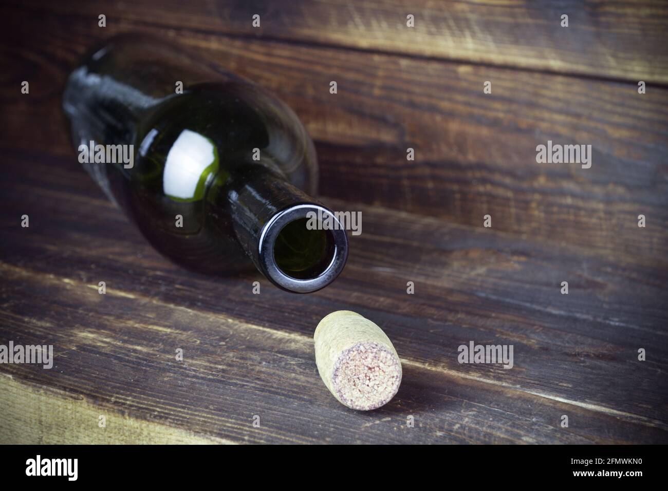 Lying empty wine bottle with cork nearby on plank wooden surface. Stock Photo